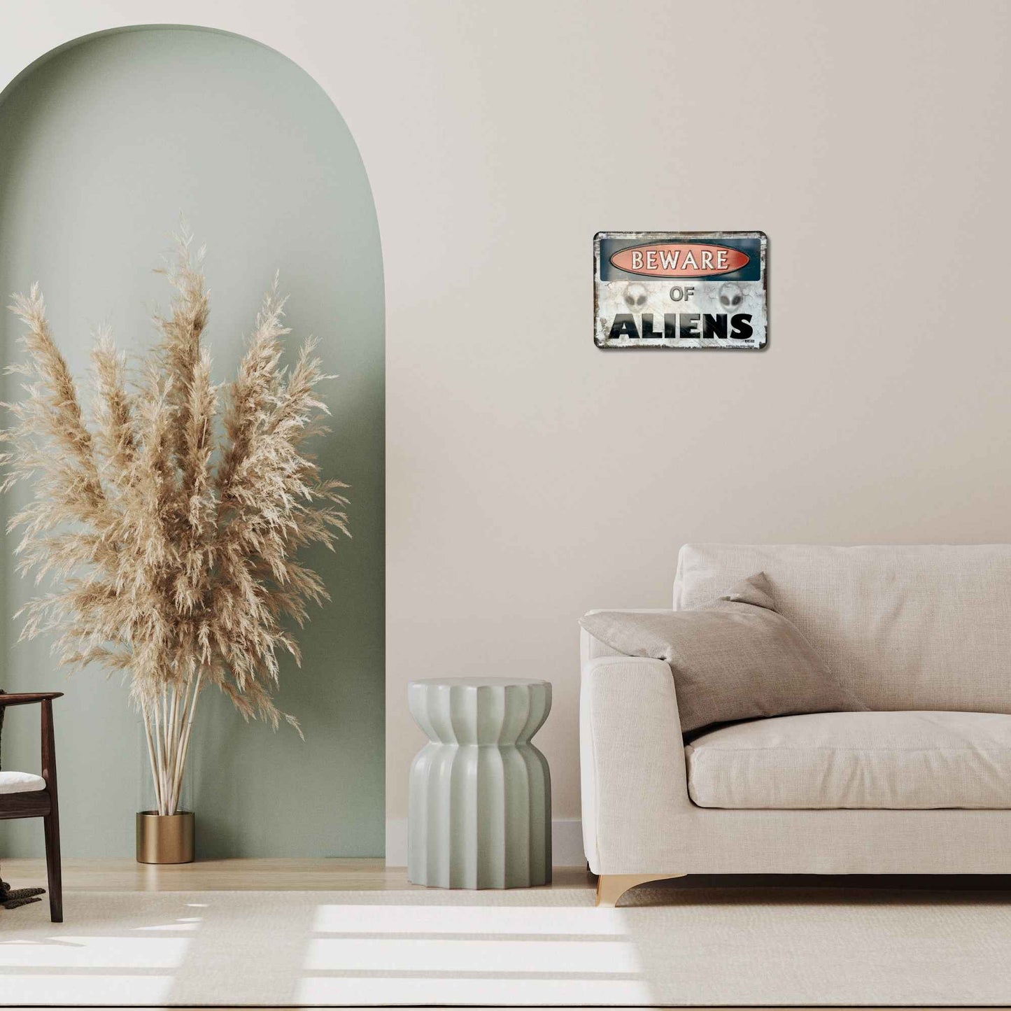 Living room with a 'Beware of Aliens' sign on the wall, pampas grass, and a beige sofa.