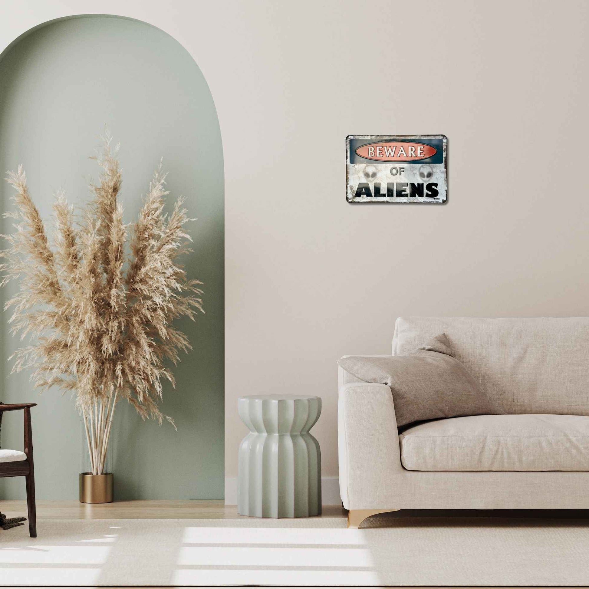 Living room with a 'Beware of Aliens' sign on the wall, pampas grass, and a beige sofa.