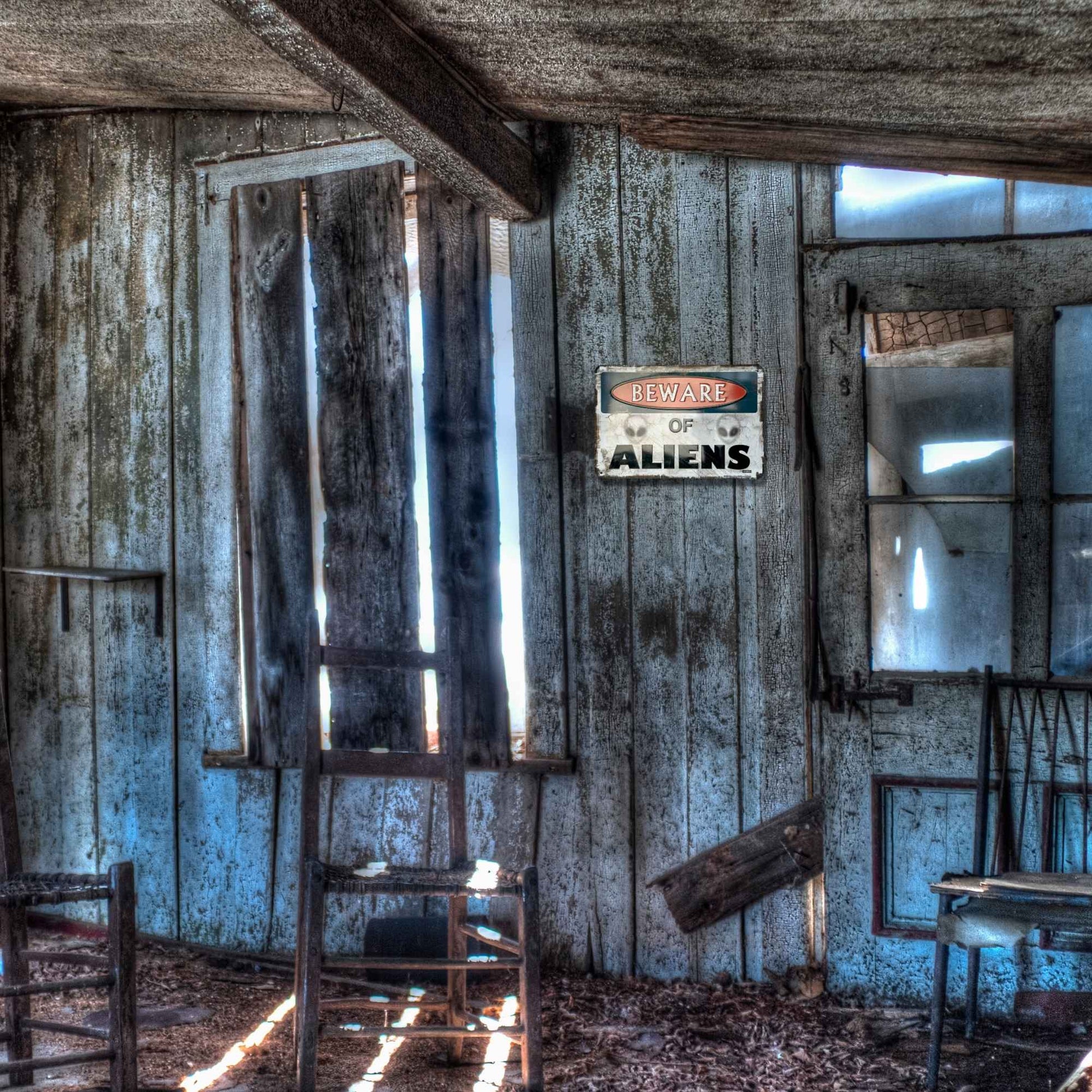 Abandoned room with peeling paint, broken windows, and a 'Wear of Aliens' sign.