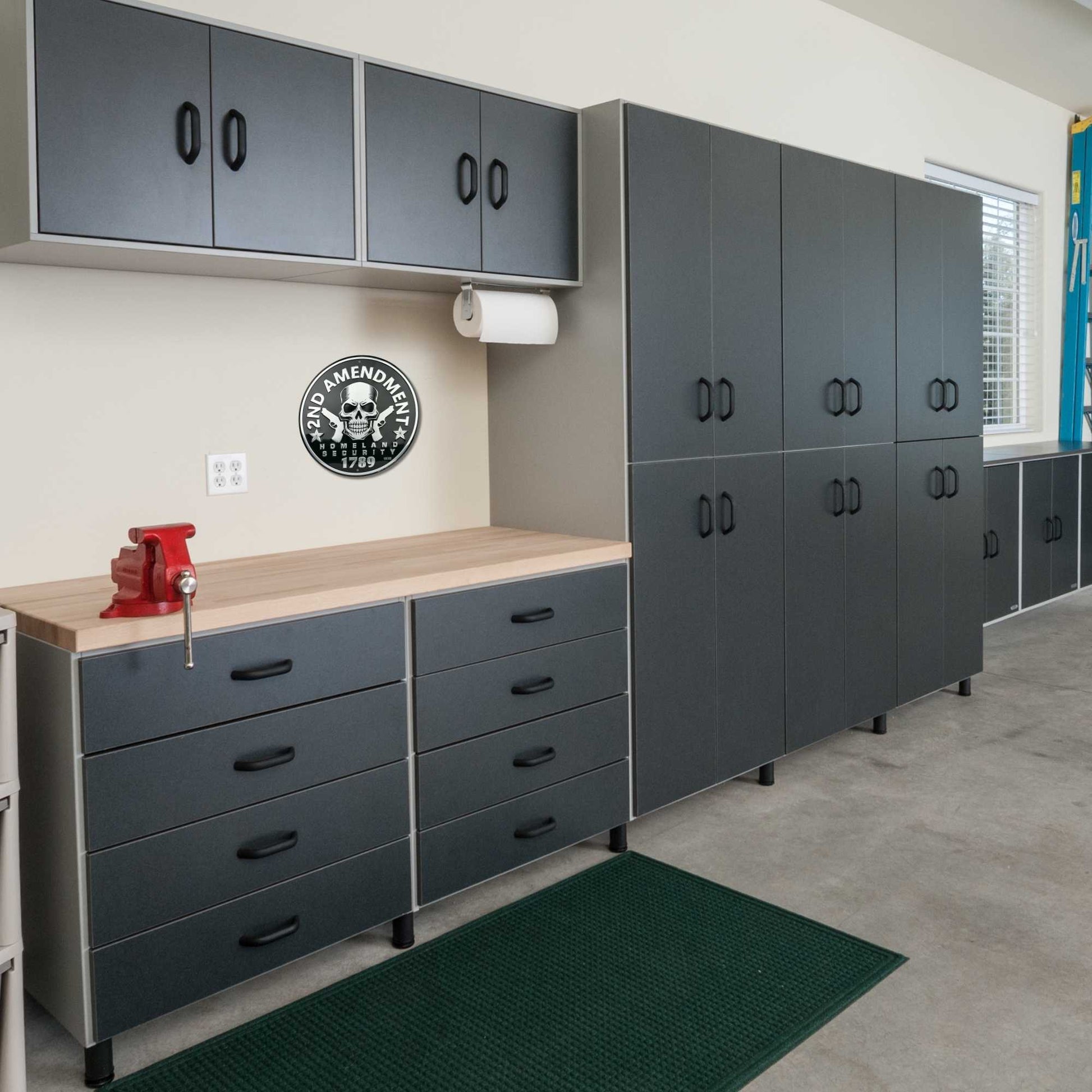 Garage interior with gray storage cabinets and drawers, a red vise, and a green mat.