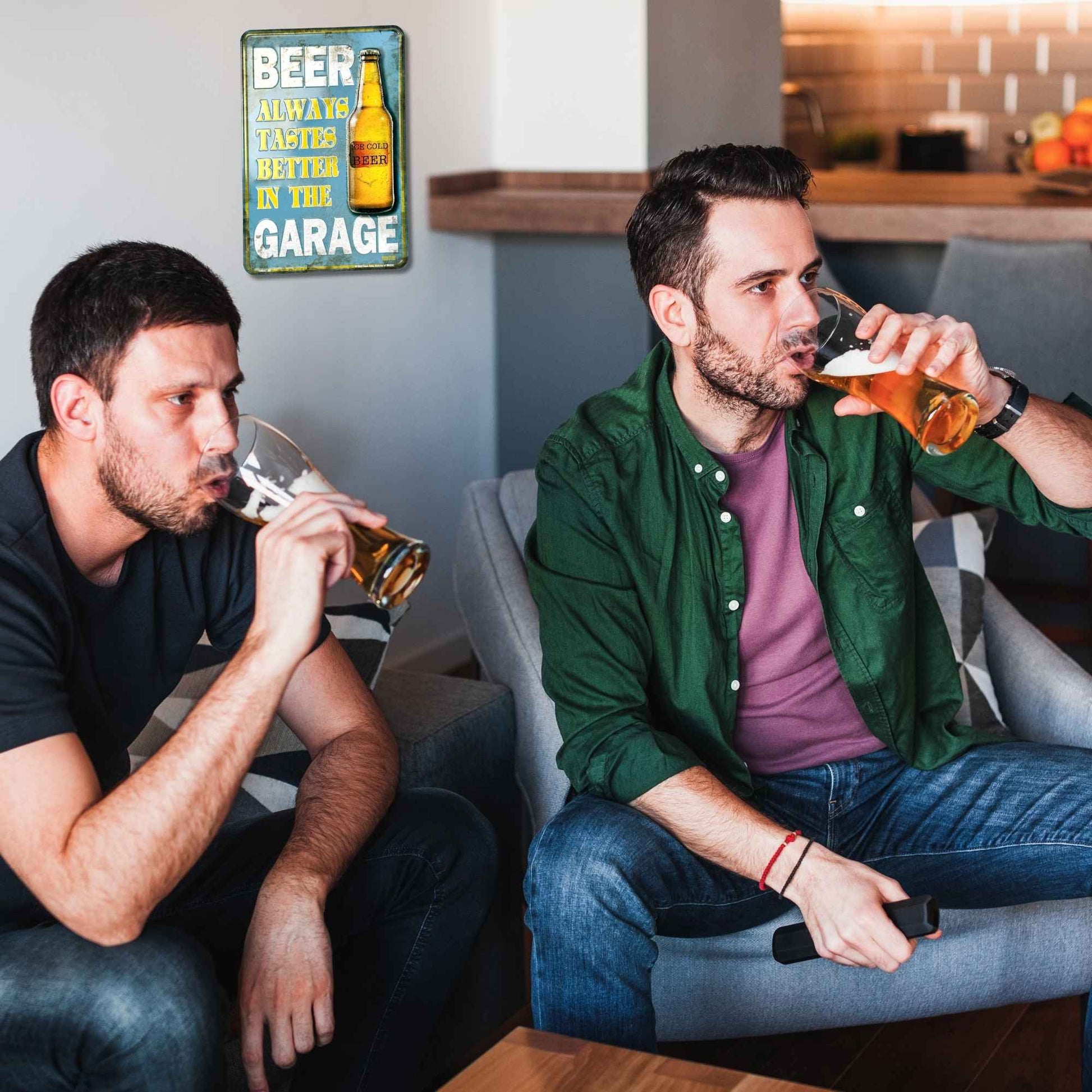 Two men sitting on a couch drinking beer with a sign in the background.