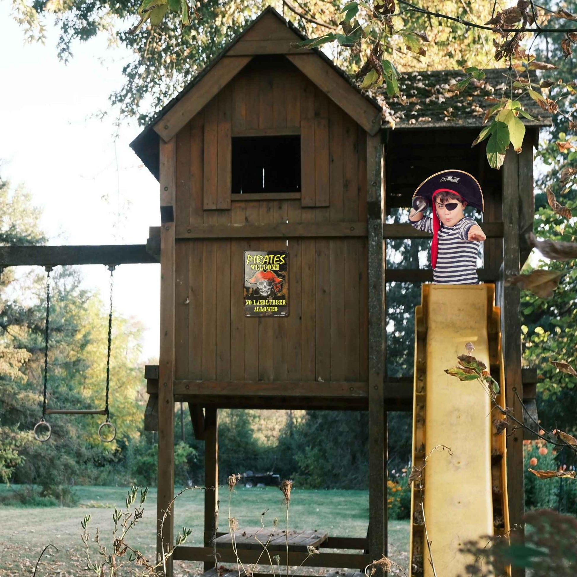 Wooden playhouse with a slide and pirate-themed decorations in a park setting.