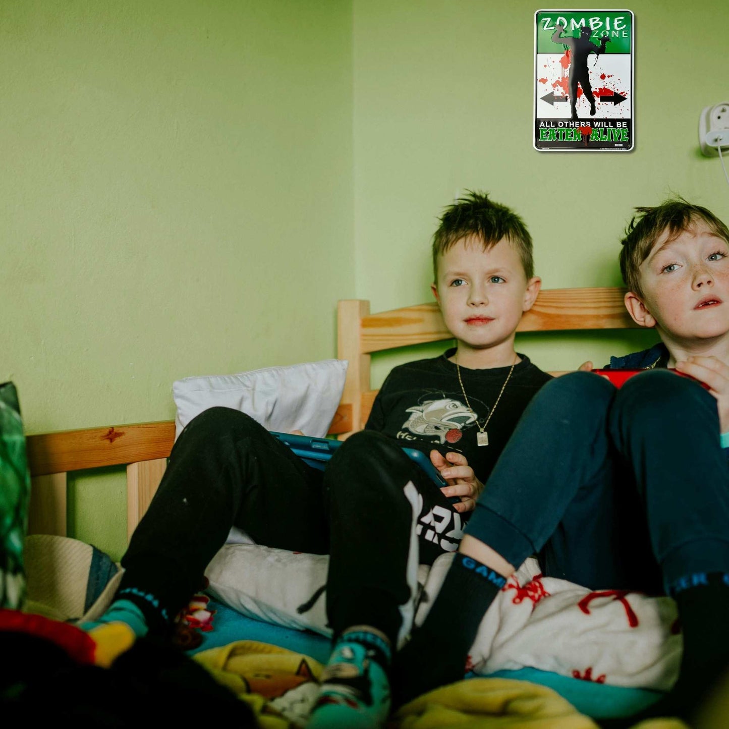 Two children sitting on a bed with a 'Zombie' movie poster on the wall.