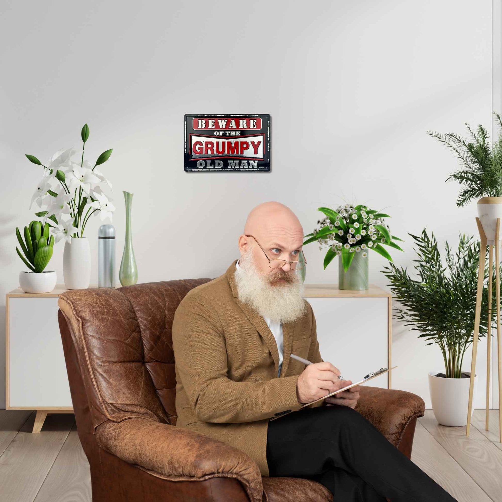 Man sitting on a brown leather armchair with a 'Beware of the Grumpy Old Man' sign in the background.
