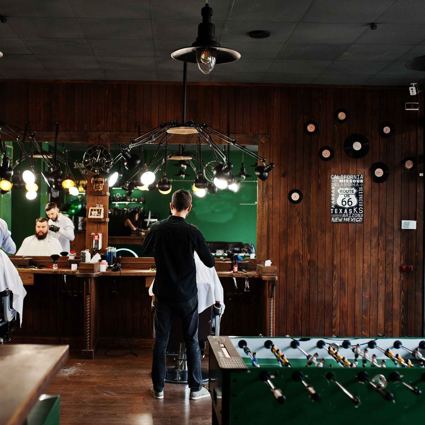 Barbershop interior with barbers and customers, vintage decor, and a foosball table.